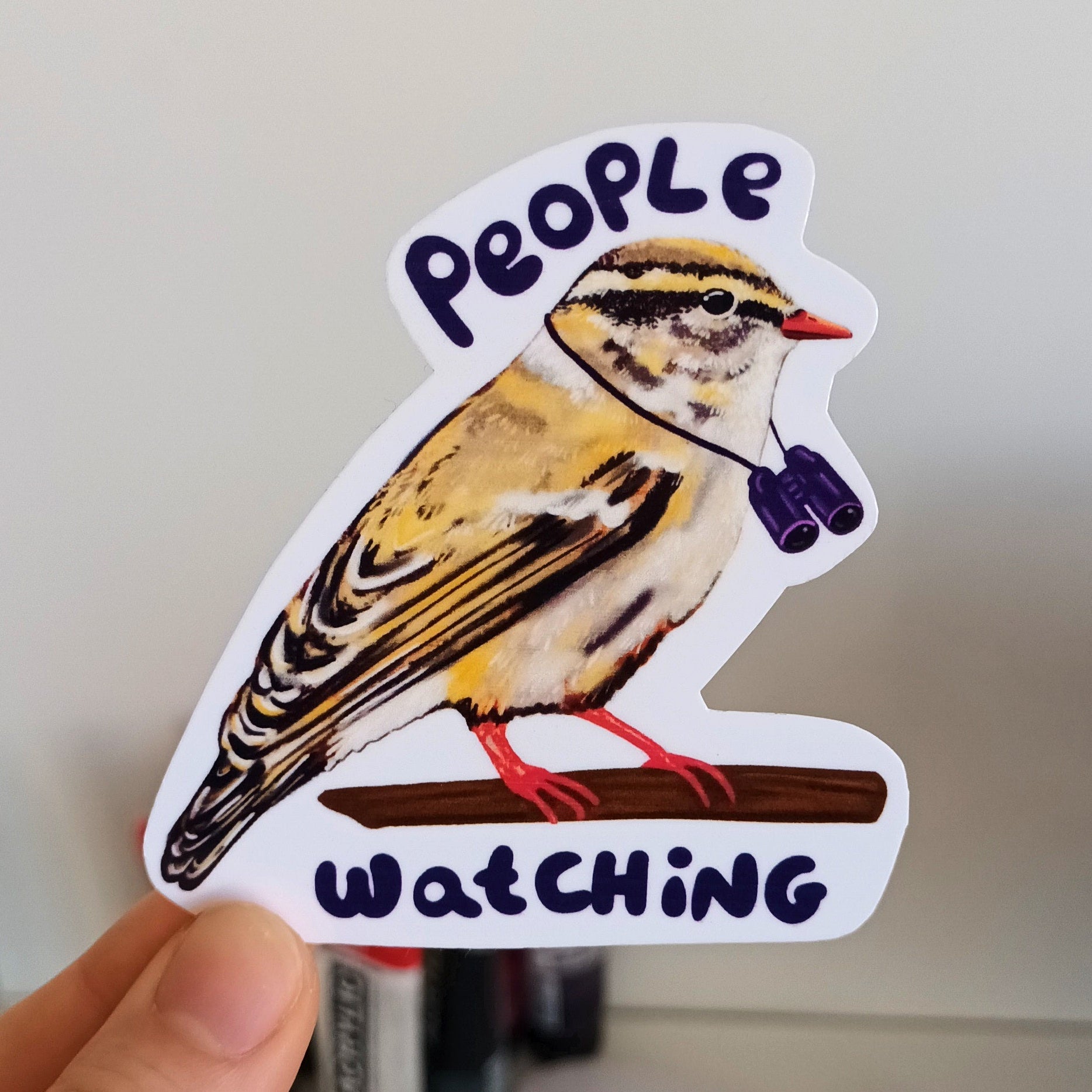 Sticker of a bird with 'People Watching' text held by a hand.