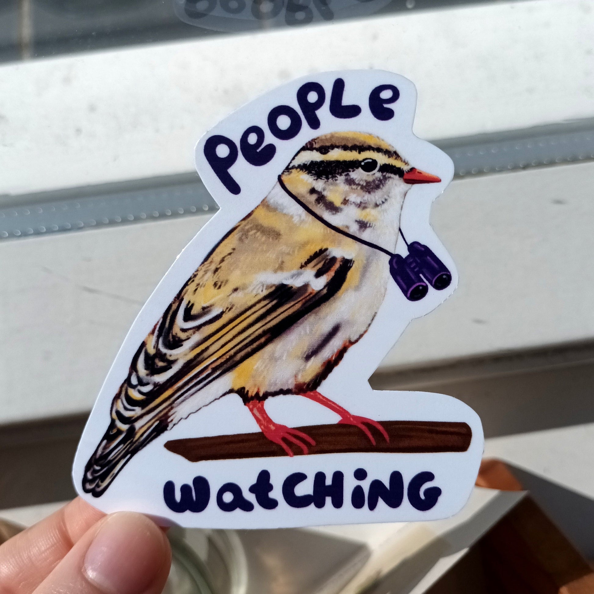 Bird sticker with 'People Watching' text held by a hand .