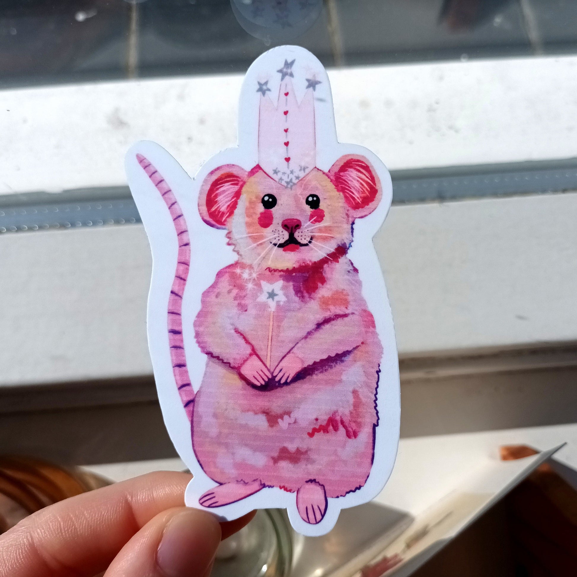 Hand holding a pink cartoon mouse sticker.