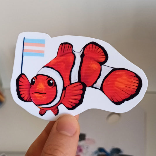 Hand holding a clownfish sticker with a trans flag.