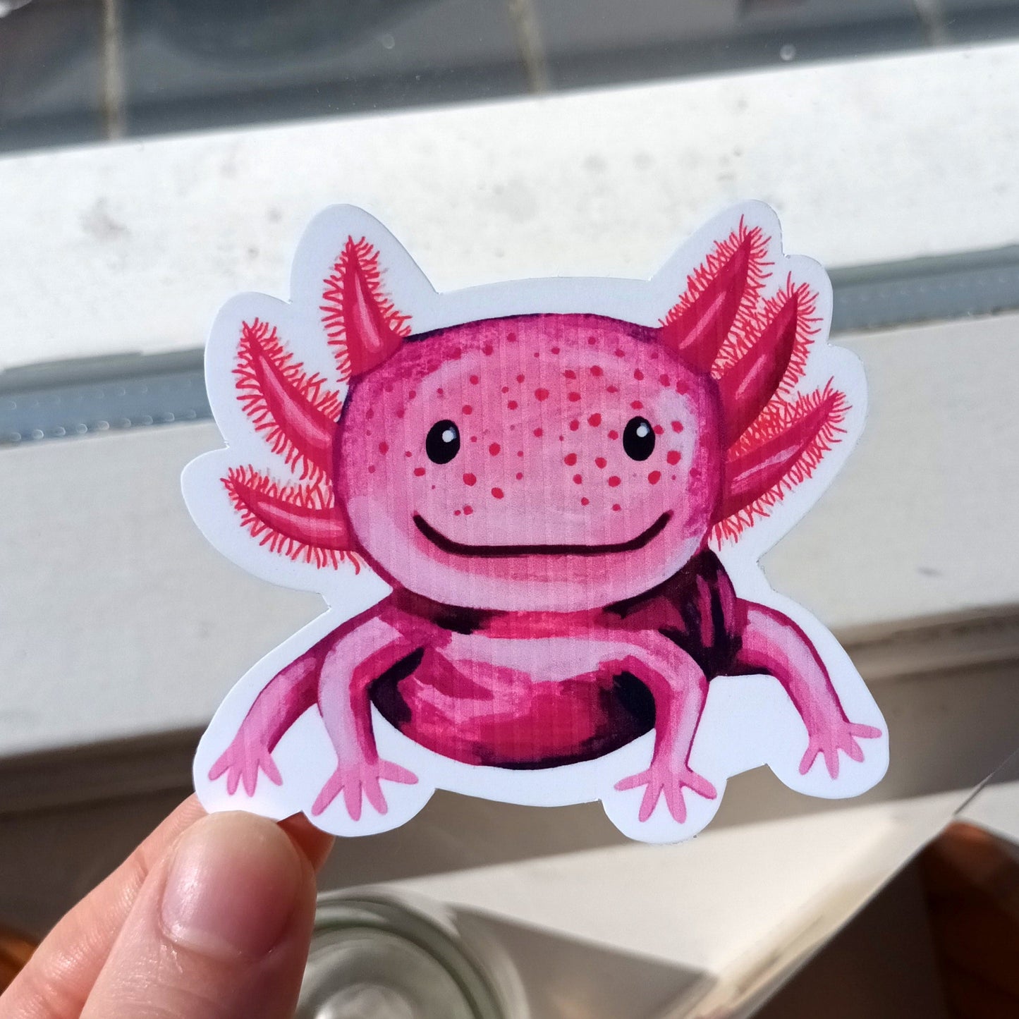 Pink axolotl sticker held by a hand .