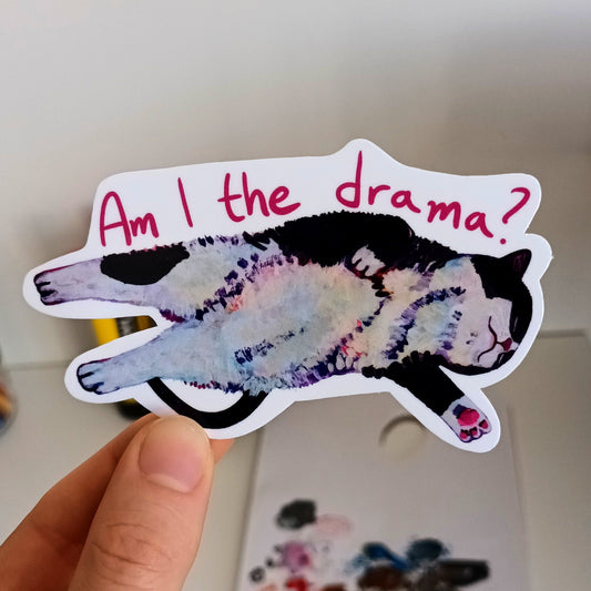 Sticker of a cat with 'Am I the drama?' text held by a hand.