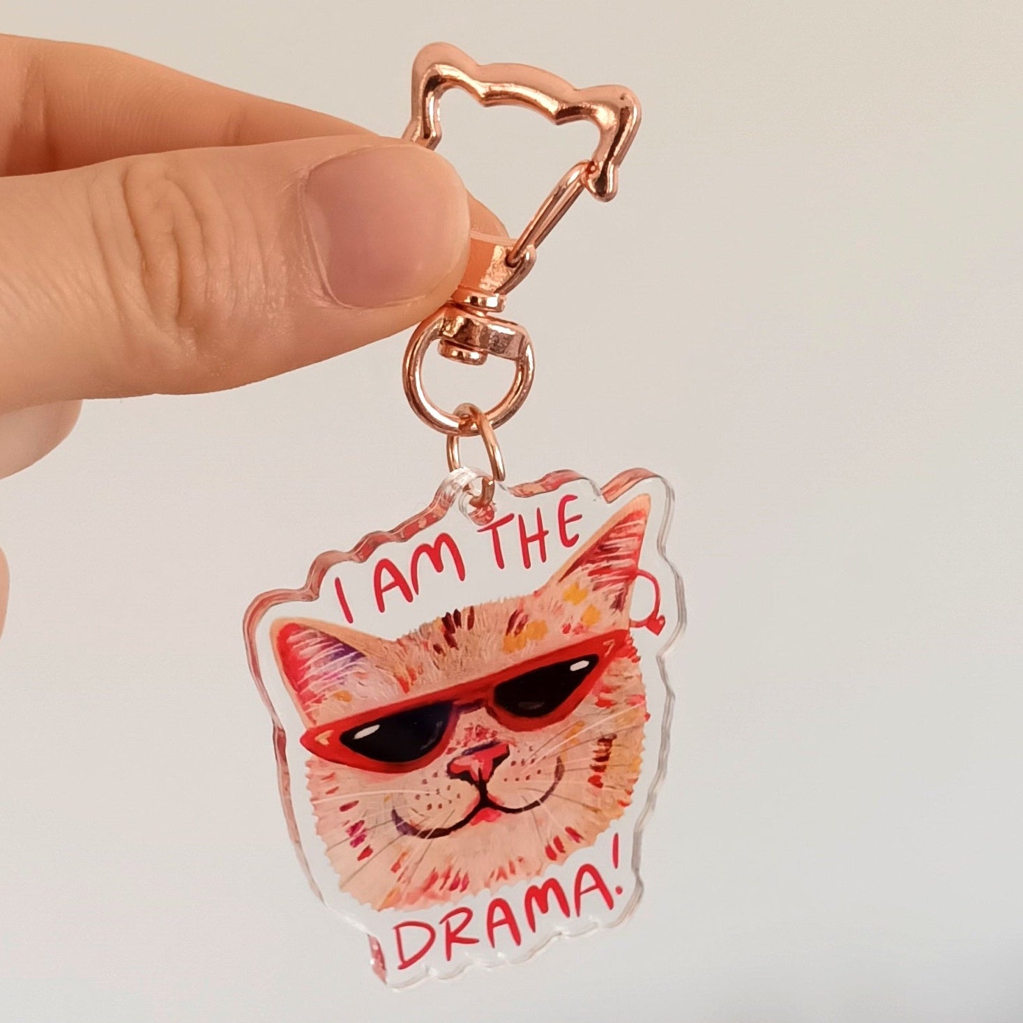 Hand holding a keychain with a I am the drama cat design and text.