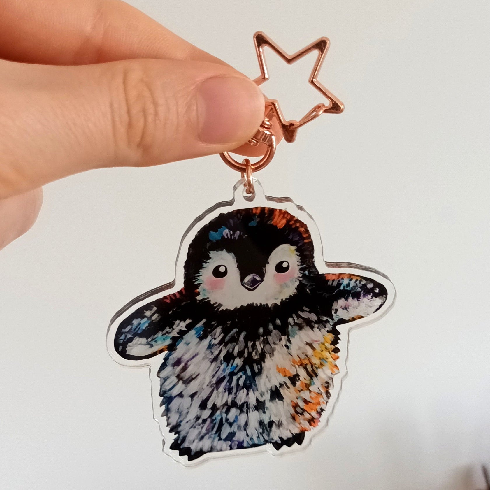 Hand holding a penguin-shaped keychain with a star charm against a white wall.