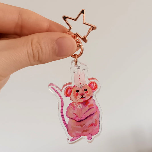 Hand holding a decorative keychain with a pink mouse design against a white background.