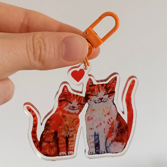 Hand holding a keychain two orange cats in love design against a white background