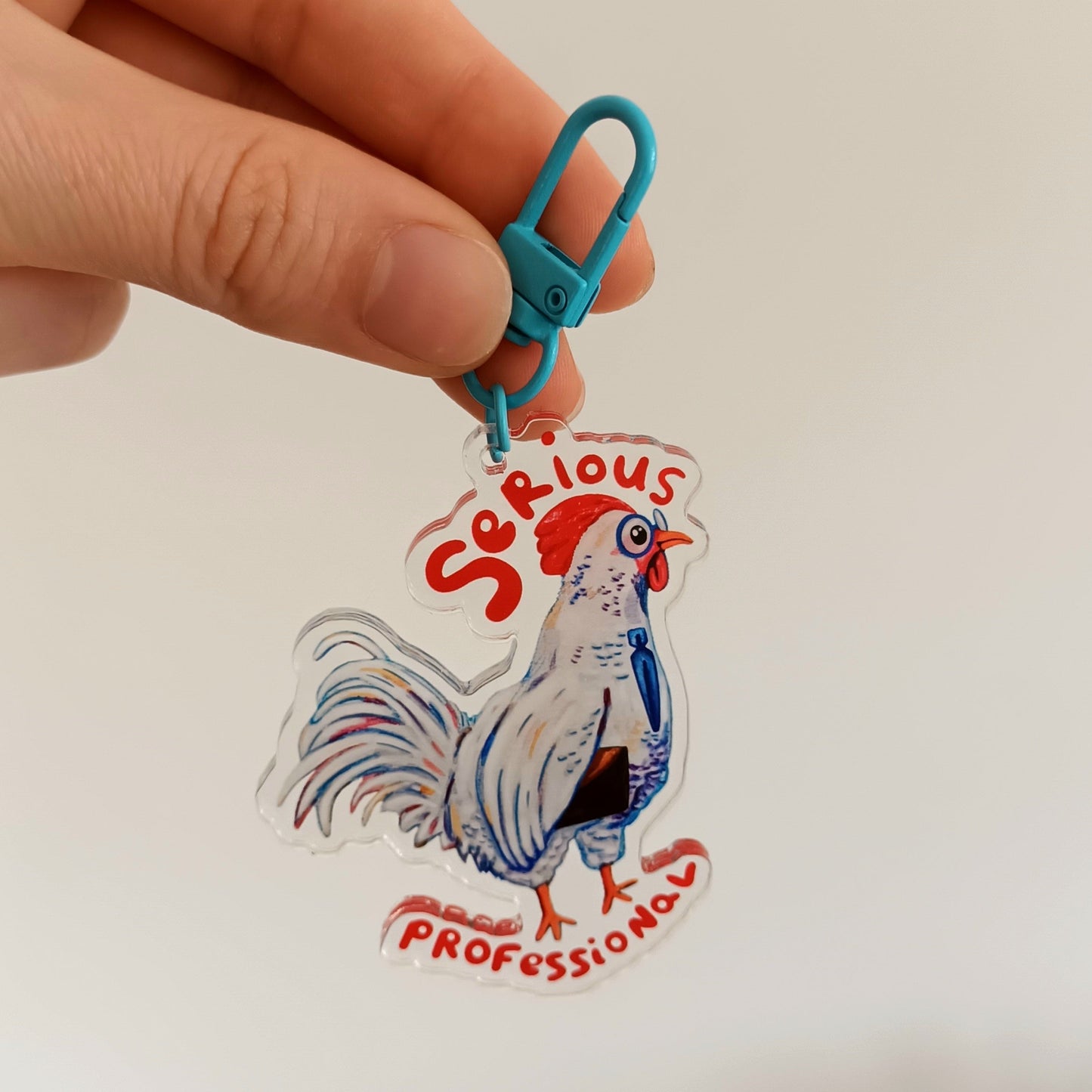 Hand holding a keychain with a rooster design and 'Serious Professional' text against a blurred background.