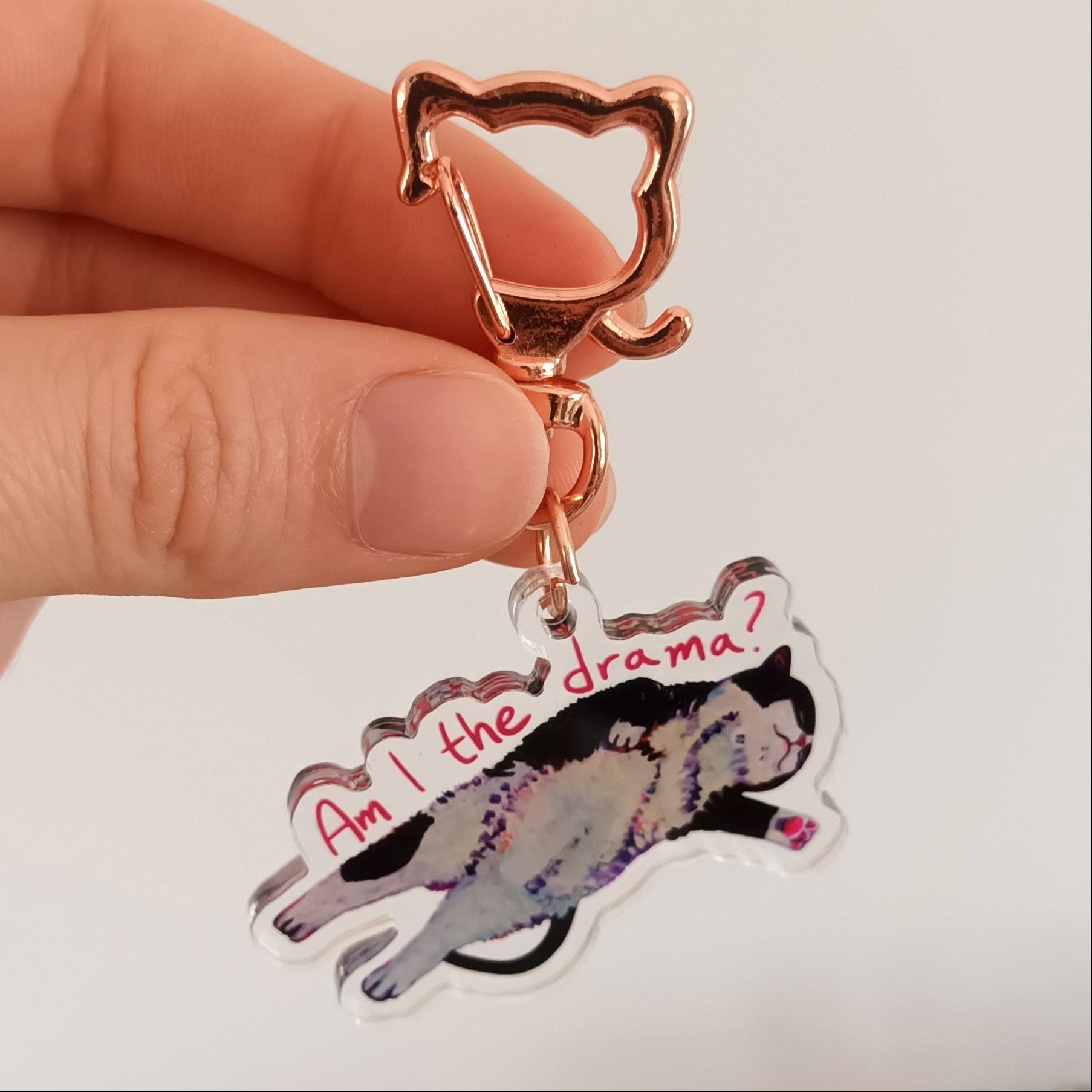 Hand holding a keychain with drama cat saying "Am I the drama?".
