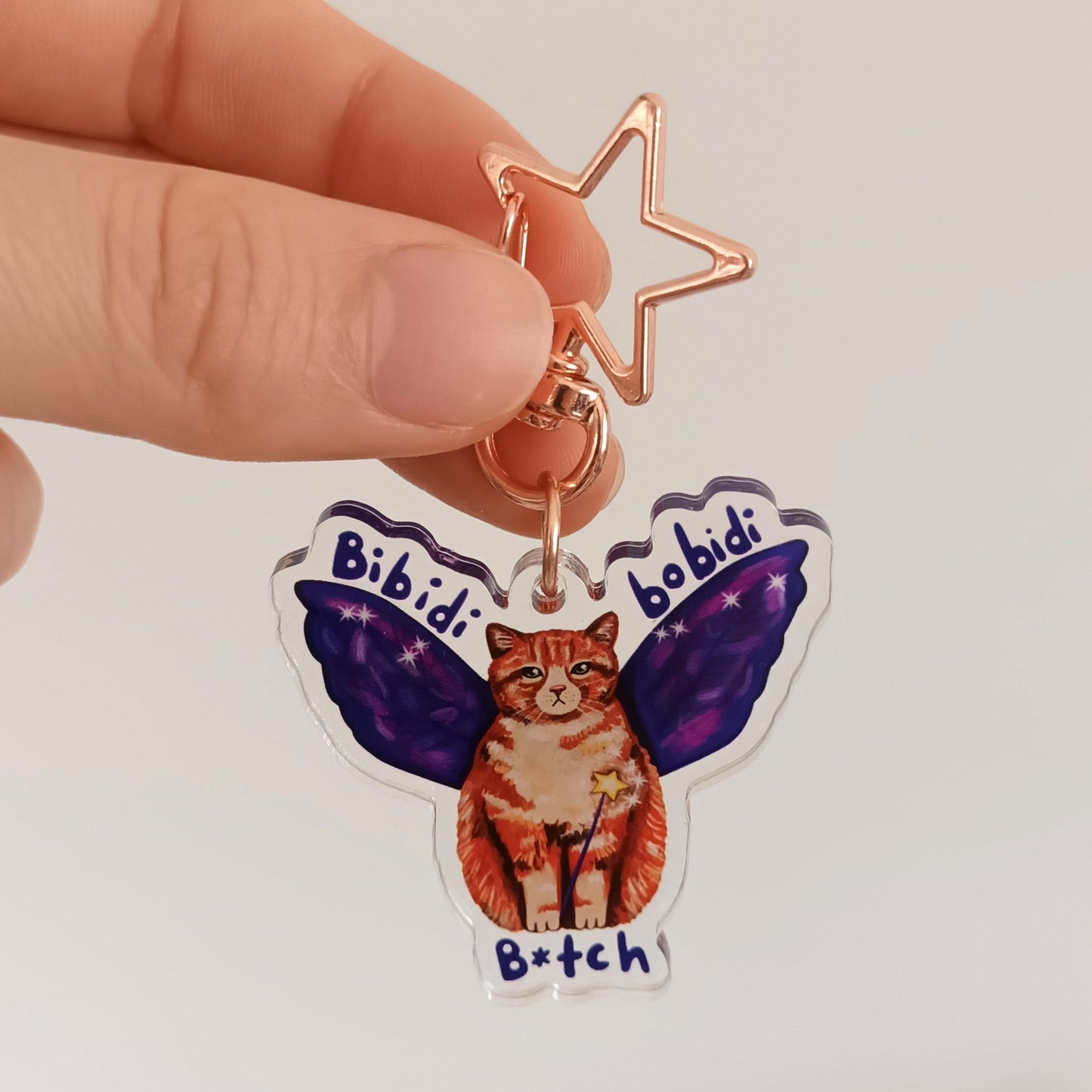 Hand holding a keychain with a cat design and text