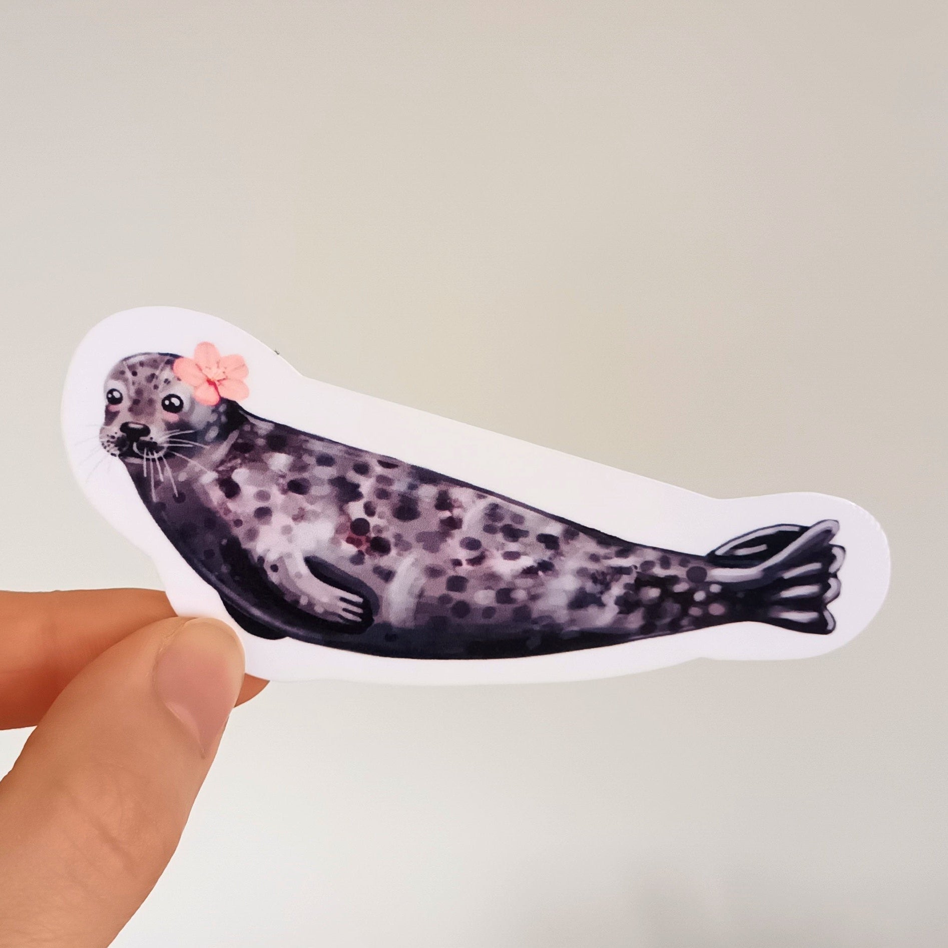 Hand holding a sticker of a seal with art supplies in the background