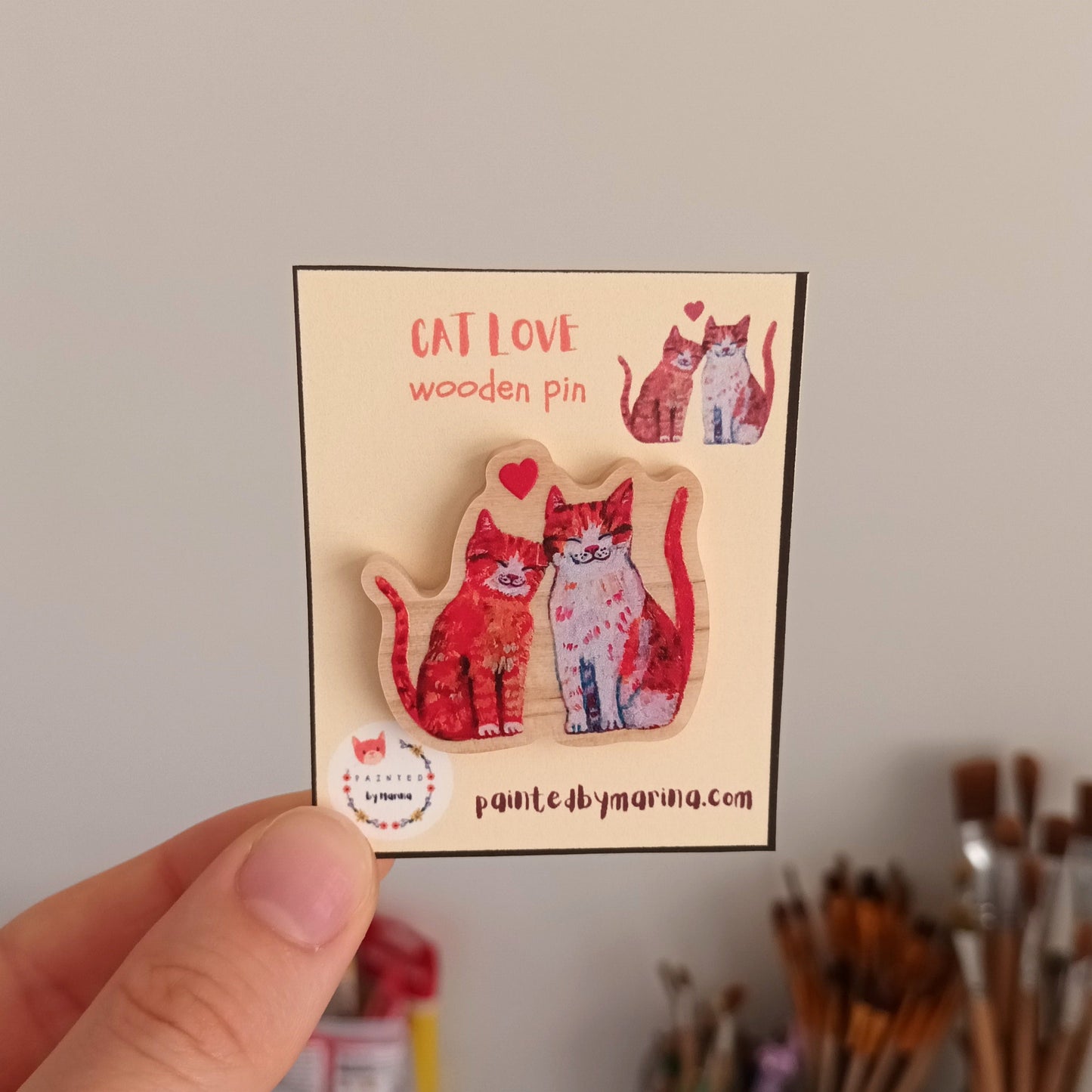 Card with cat-themed wooden pins held by a hand against a neutral background.