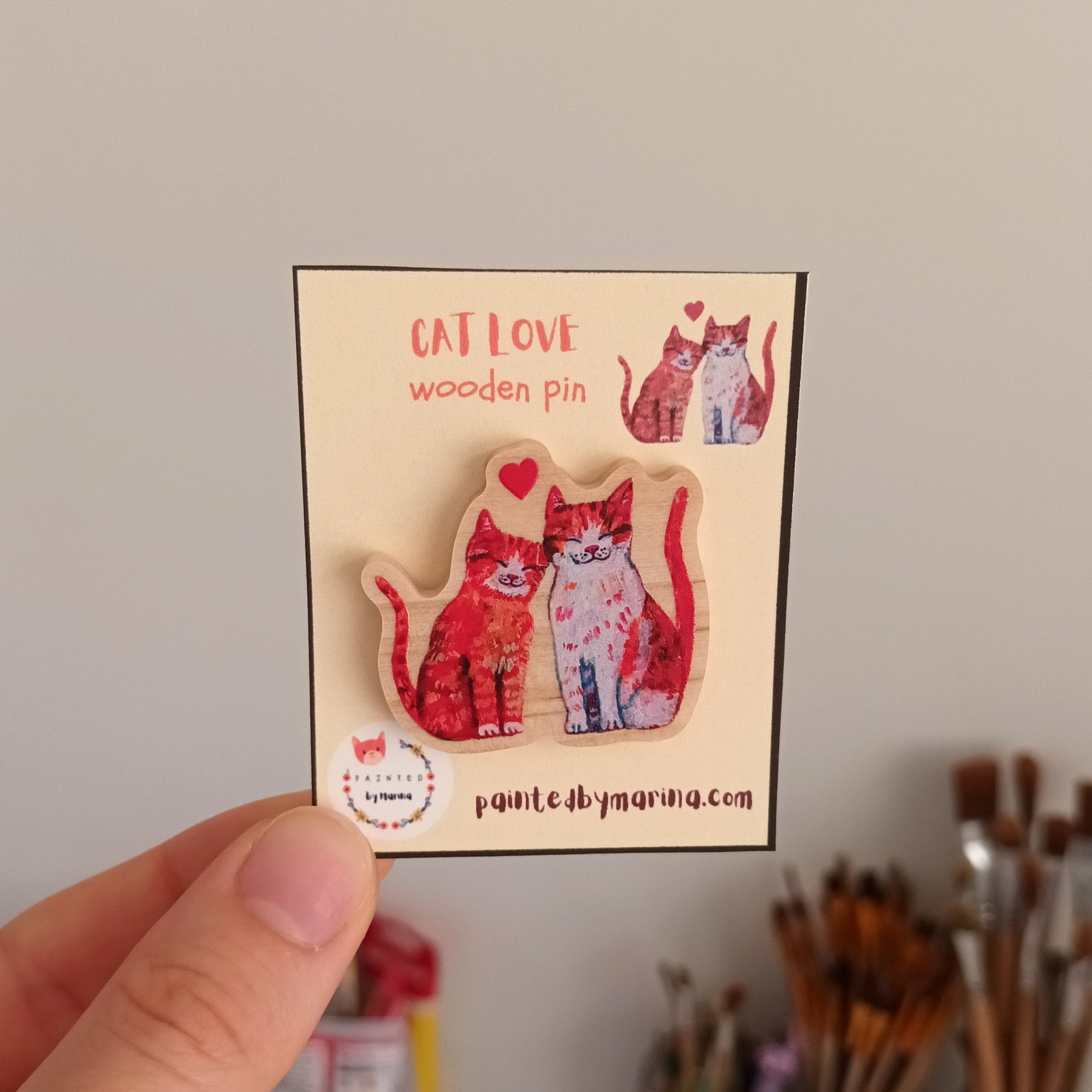 Card with cat-themed wooden pins held by a hand against a neutral background.