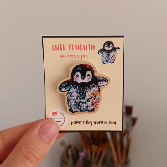 Penguin wooden pin held in front of its packaging with a white background