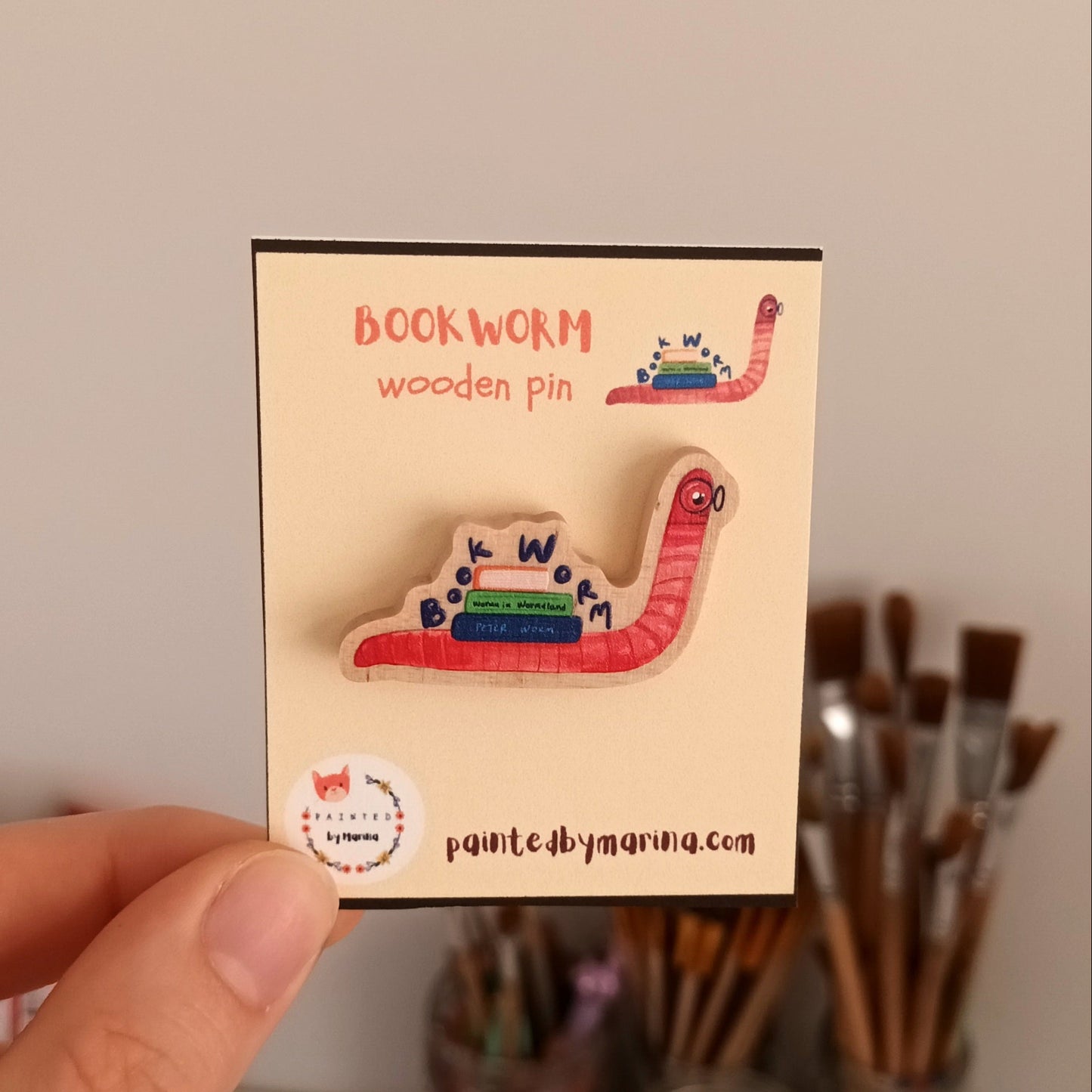 Hand holding a card with a bookworm-shaped wooden pin and 'bookworm' text.