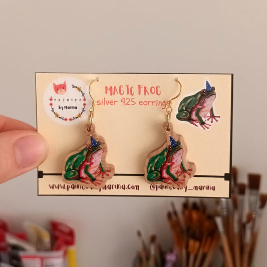 Hand holding a box of earrings with a frog design