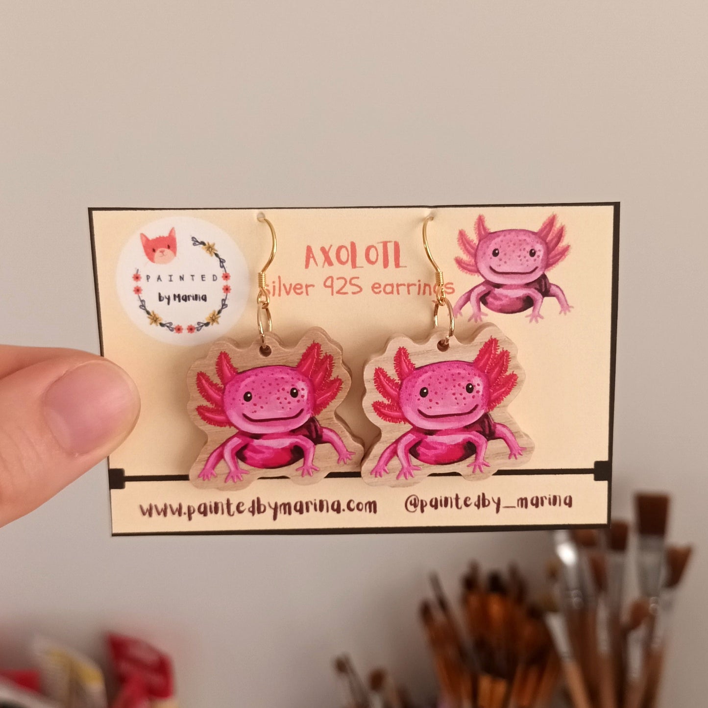 Hand holding earrings with a cute axolotl design