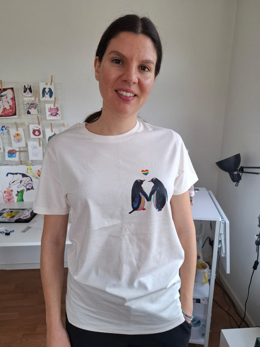 Person wearing a white t-shirt with penguins and rainbow heart design 