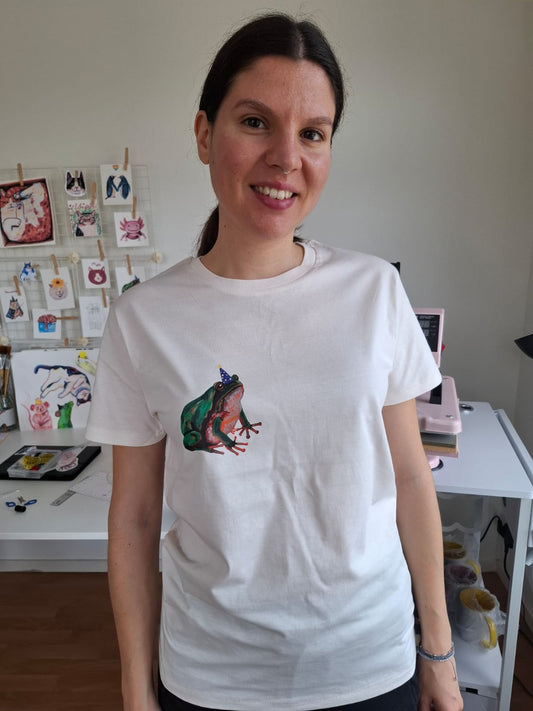 Person wearing a white t-shirt with a colorful frog design in an indoor setting.