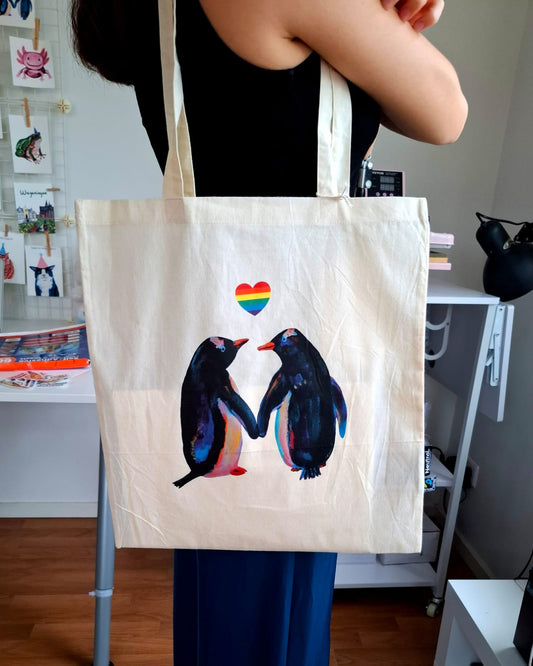 Organic cotton tote bag with two penguins holding a rainbow heart, LGBTQ+ pride design.