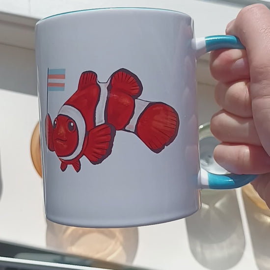 Video of cute clownfish holding transgender pride flag on handmade mug with blue handle