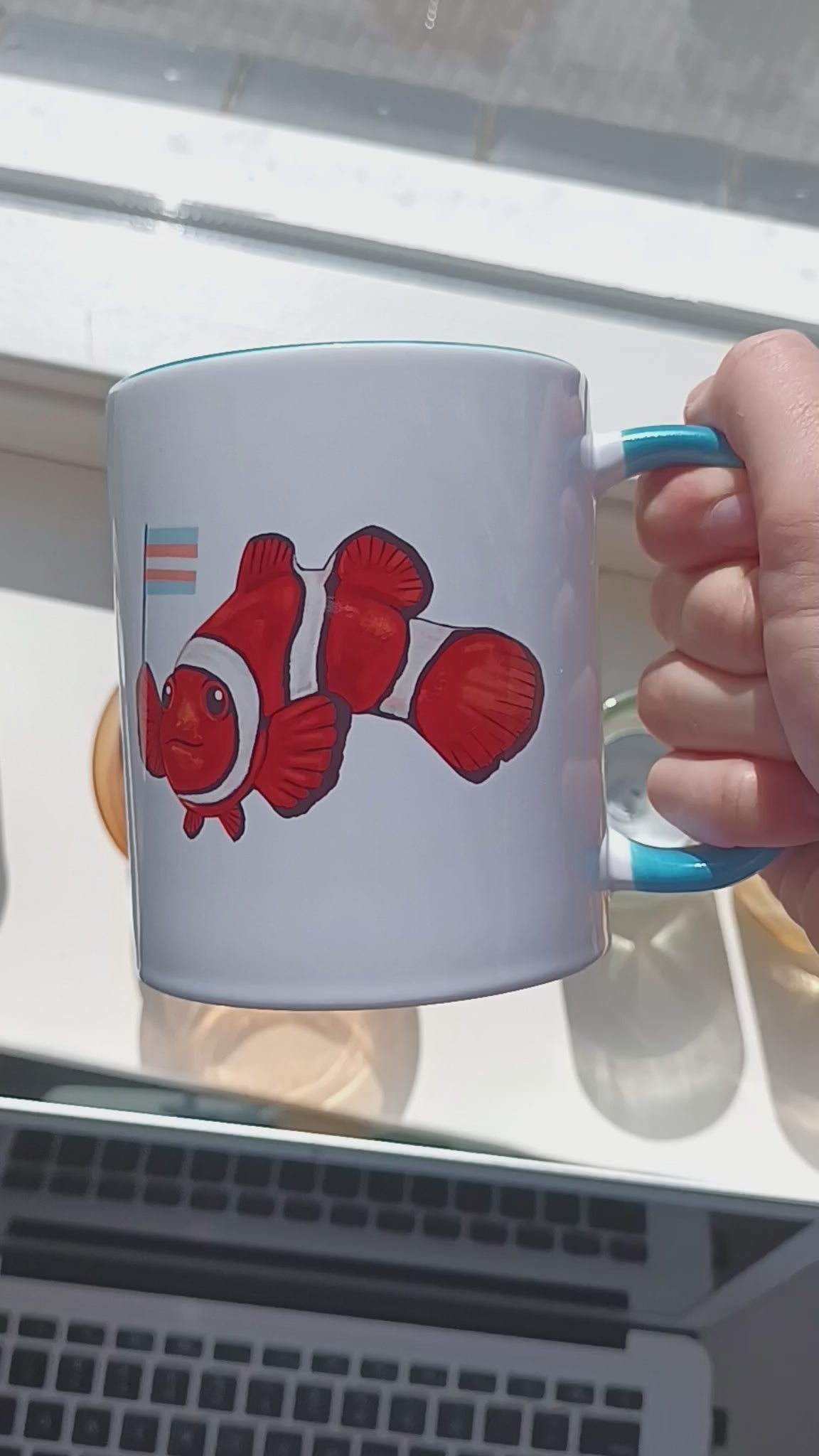 Video of cute clownfish holding transgender pride flag on handmade mug with blue handle